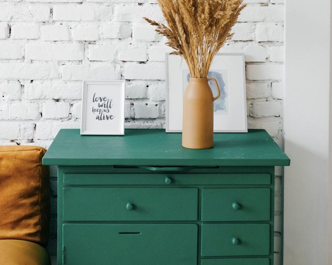 A green living room table with some paintings and a flower vase above it